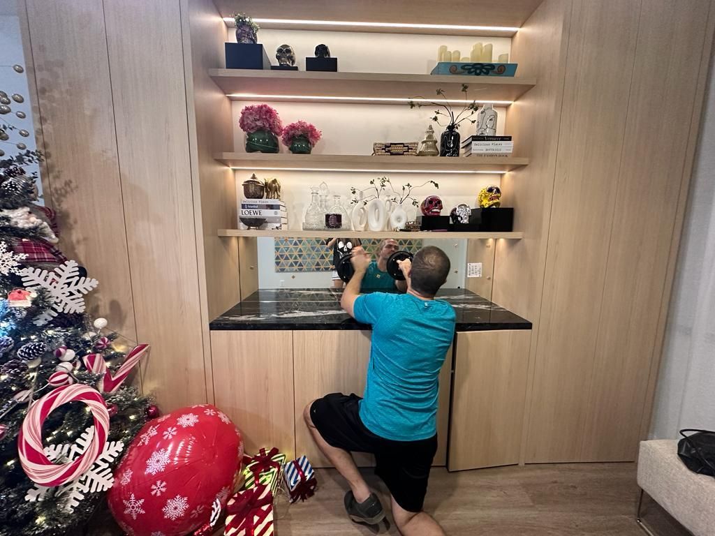 A man is kneeling down in front of a christmas tree in a living room.