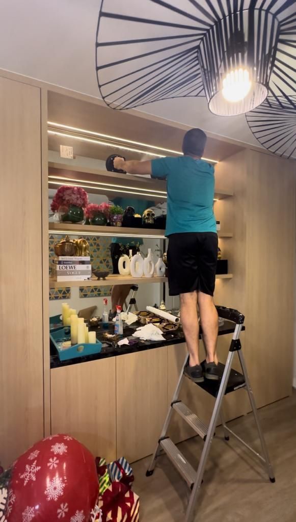 A man is standing on a ladder cleaning a shelf.