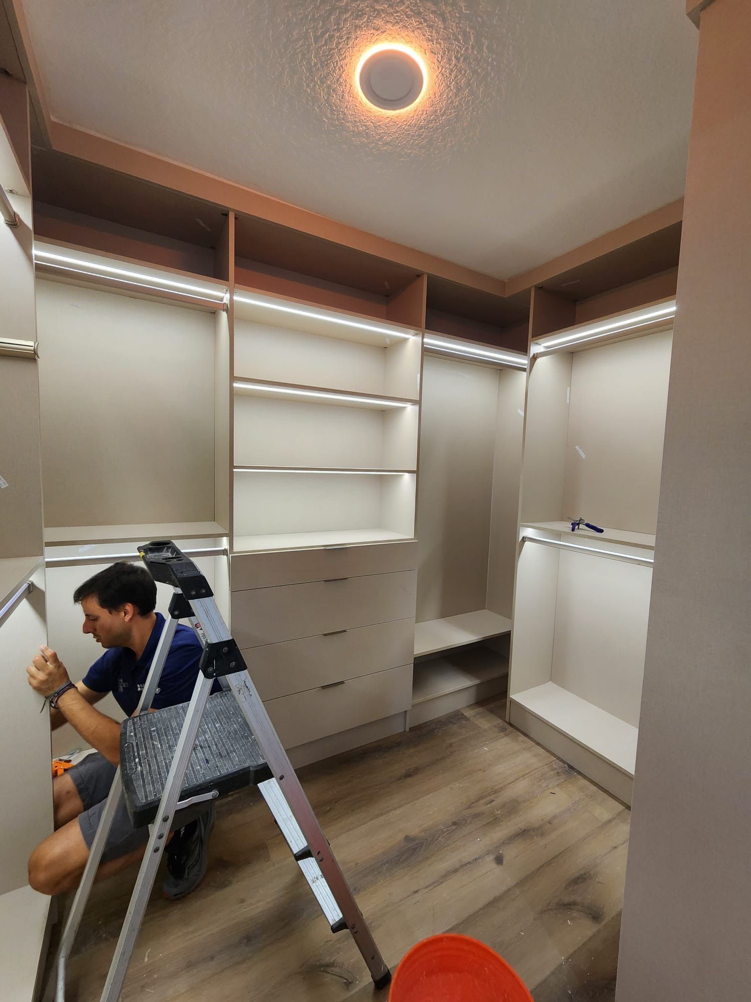 A man is sitting on a ladder in a walk in closet.