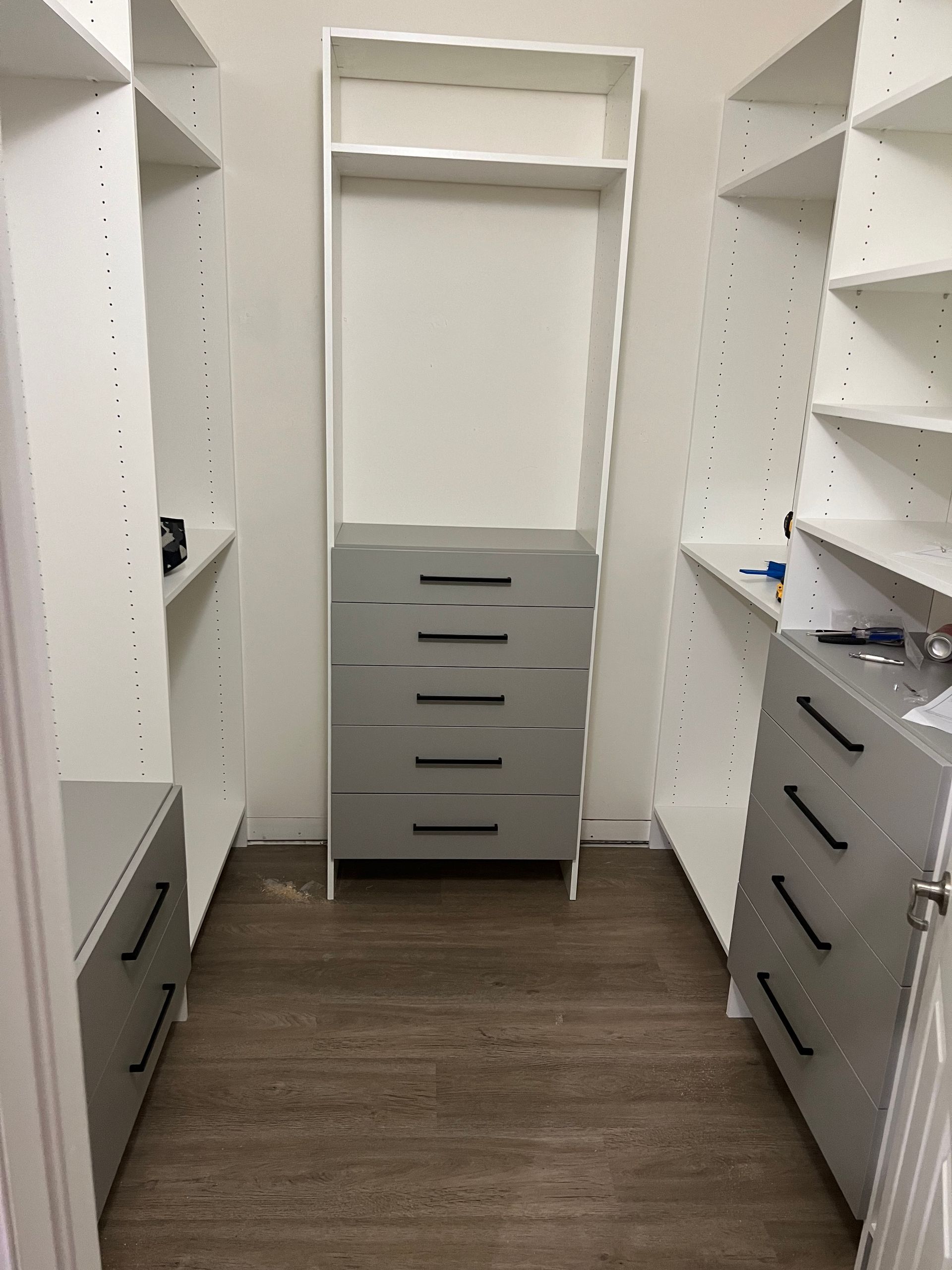 A walk in closet with white shelves and gray drawers.