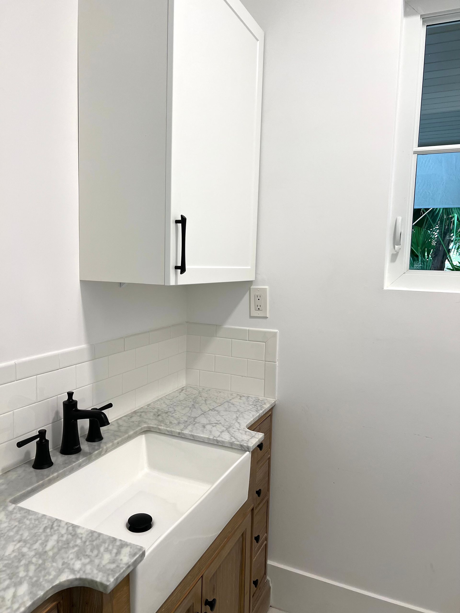 A bathroom with a sink , cabinets , and a window.