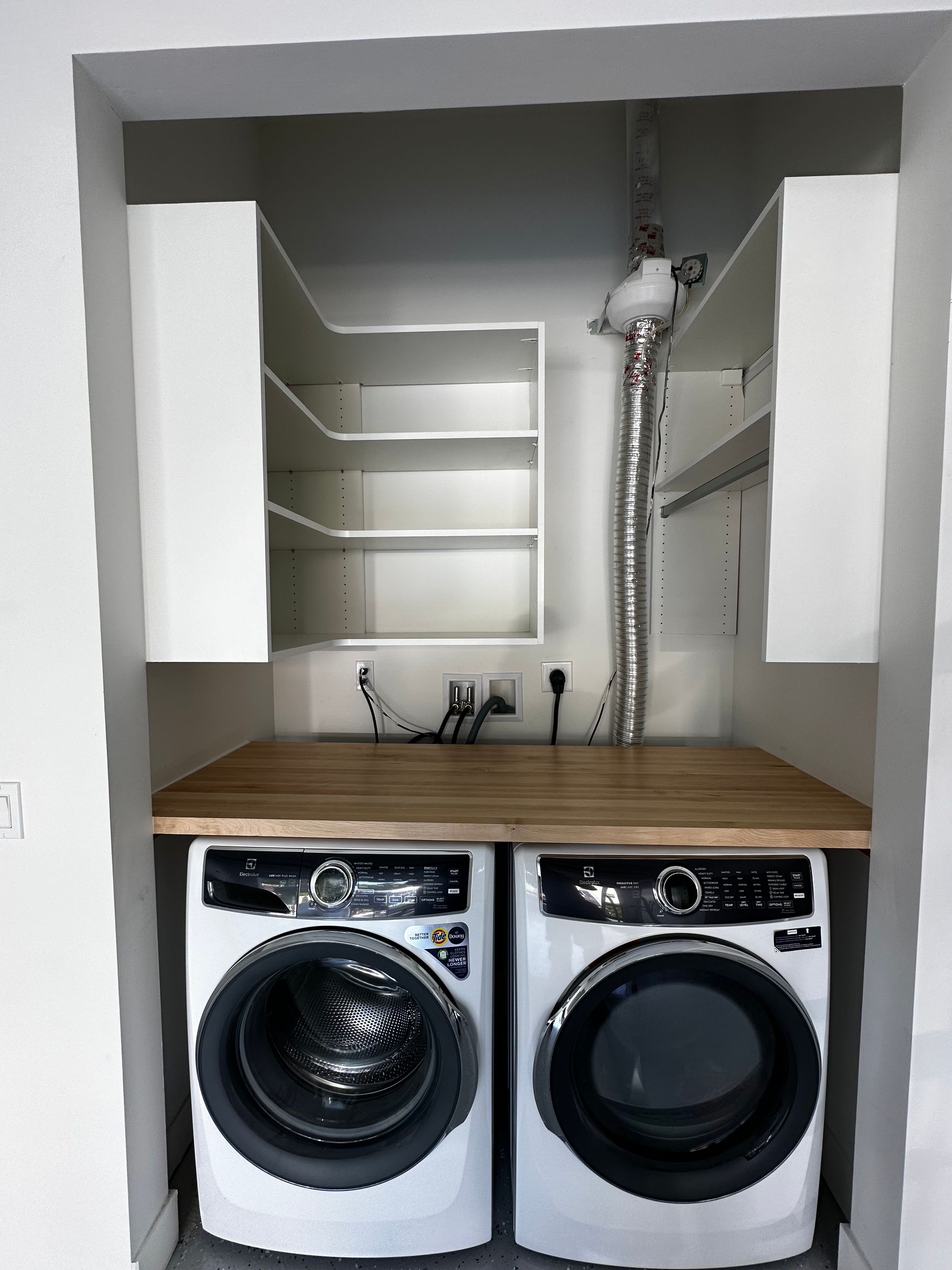 A laundry room with two washers and dryers under a wooden table