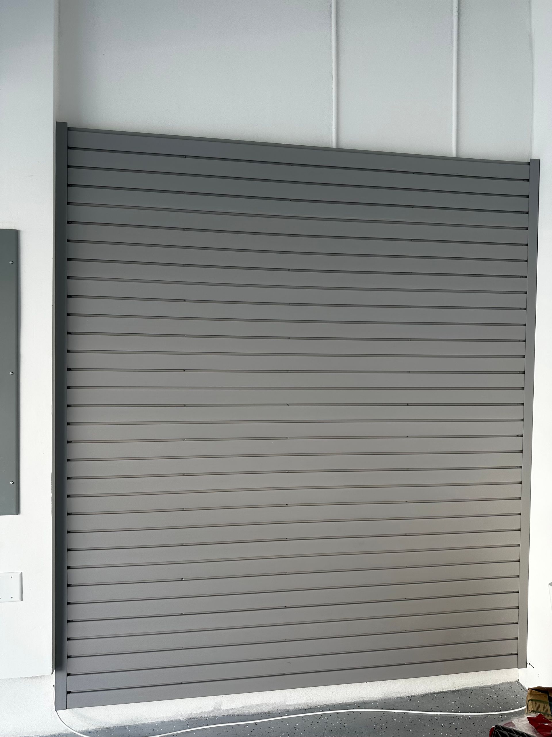 A gray garage slatwall  sitting on a white wall.