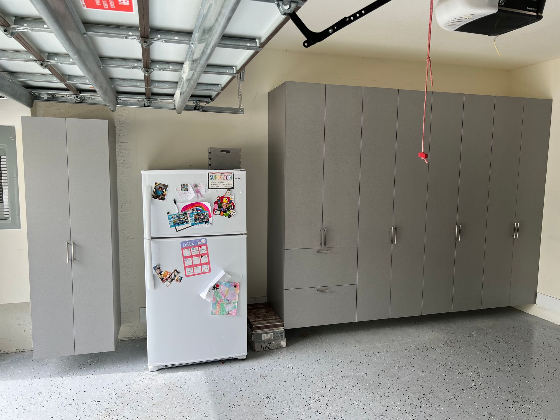 A refrigerator in a garage with a lot of cabinets.