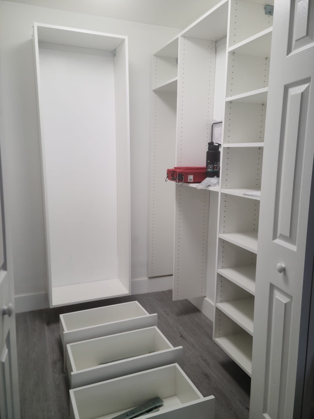 A white walk in closet with lots of shelves and drawers.
