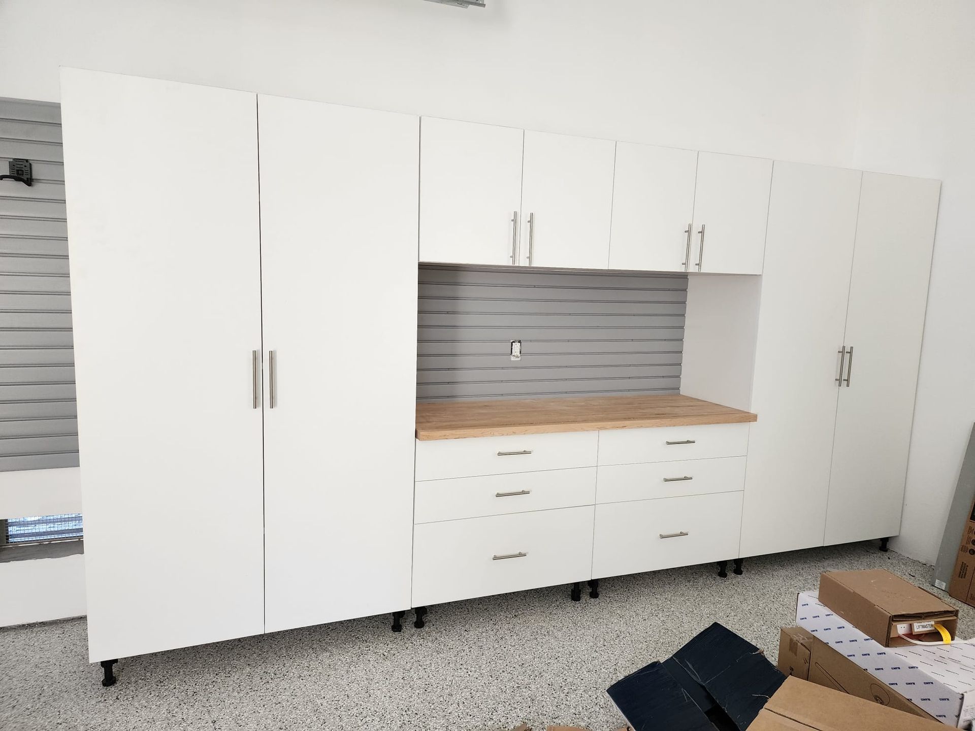 A white garage cabinet counter top workbench and a slatwall in the middle