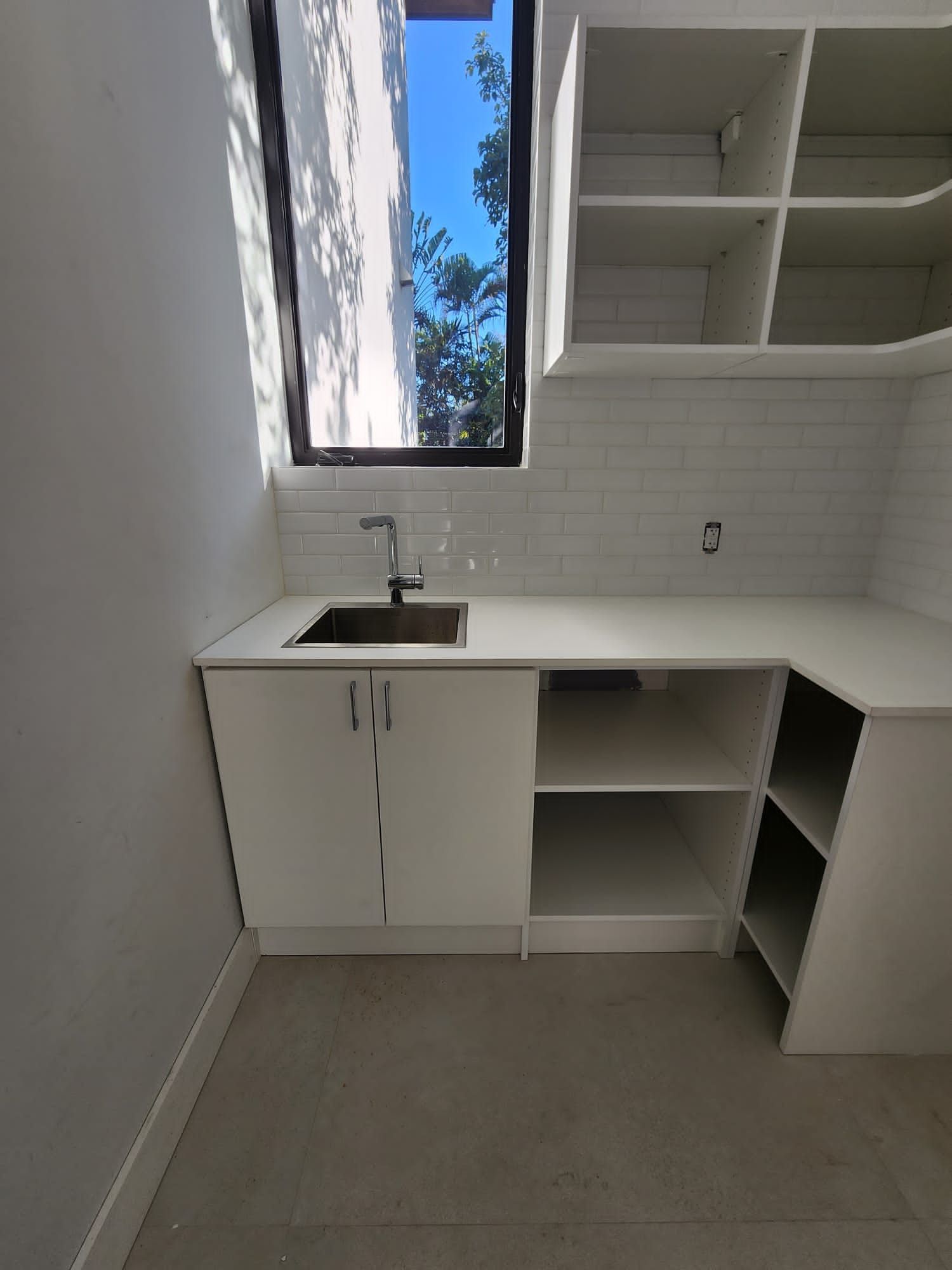 A kitchen with a sink , cabinets , shelves and a window.