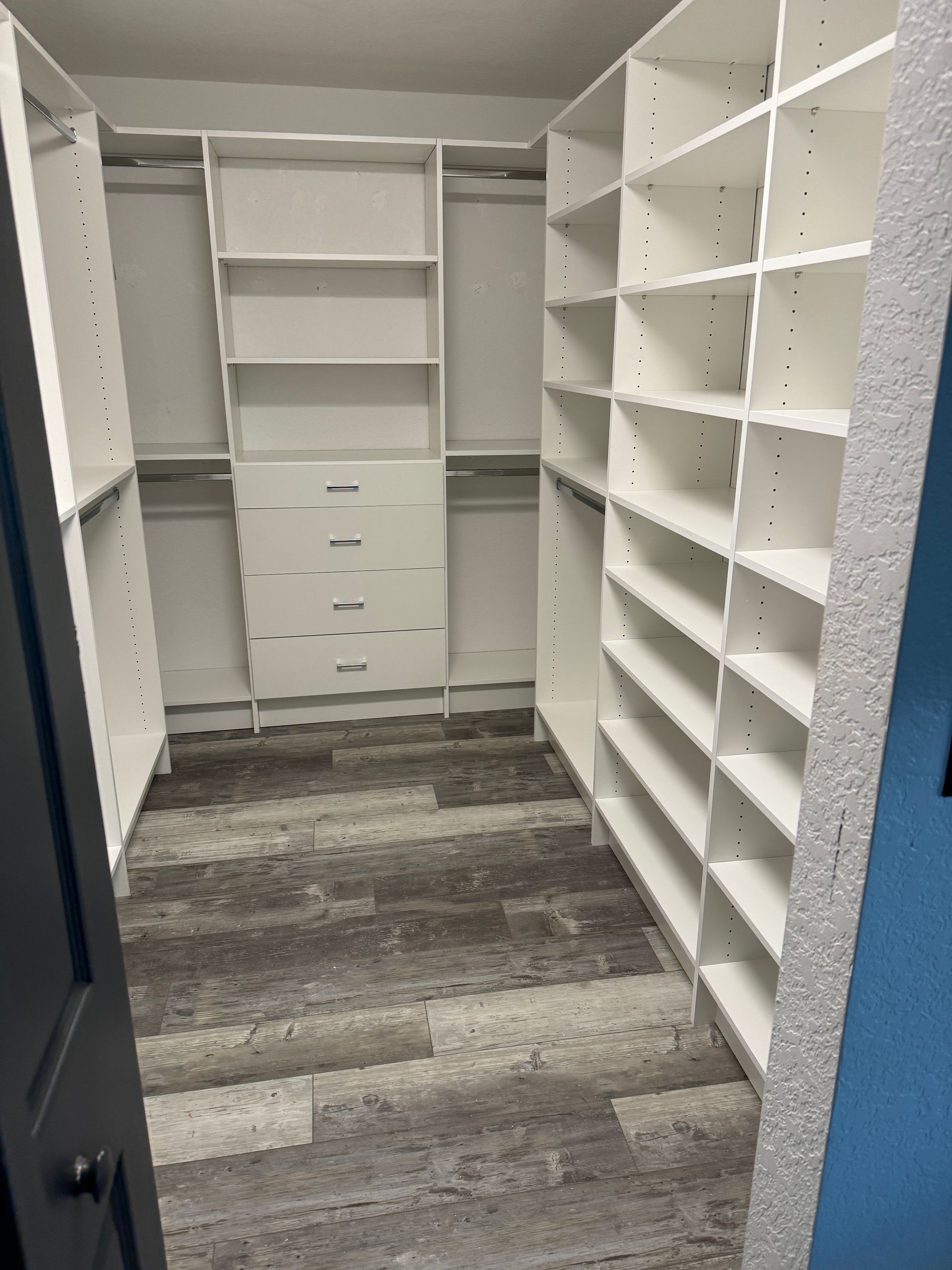 A walk in closet with white shelves and gray drawers.