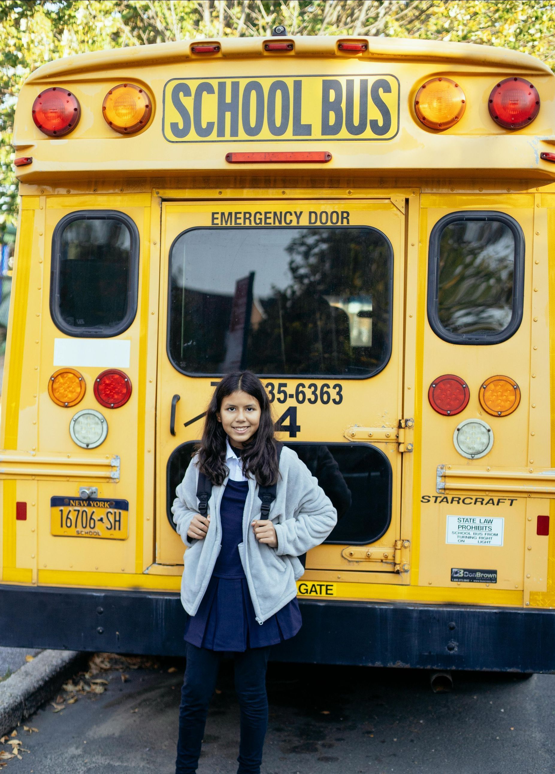 A girl is standing in front of a yellow school bus.