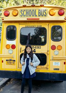 A girl is standing in front of a yellow school bus.