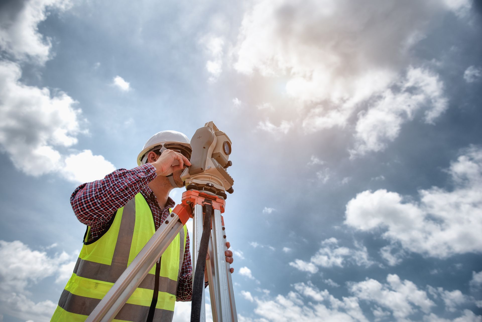 A QS surveyor wearing a vest and a helmet is at a construction site performing surveying services.
