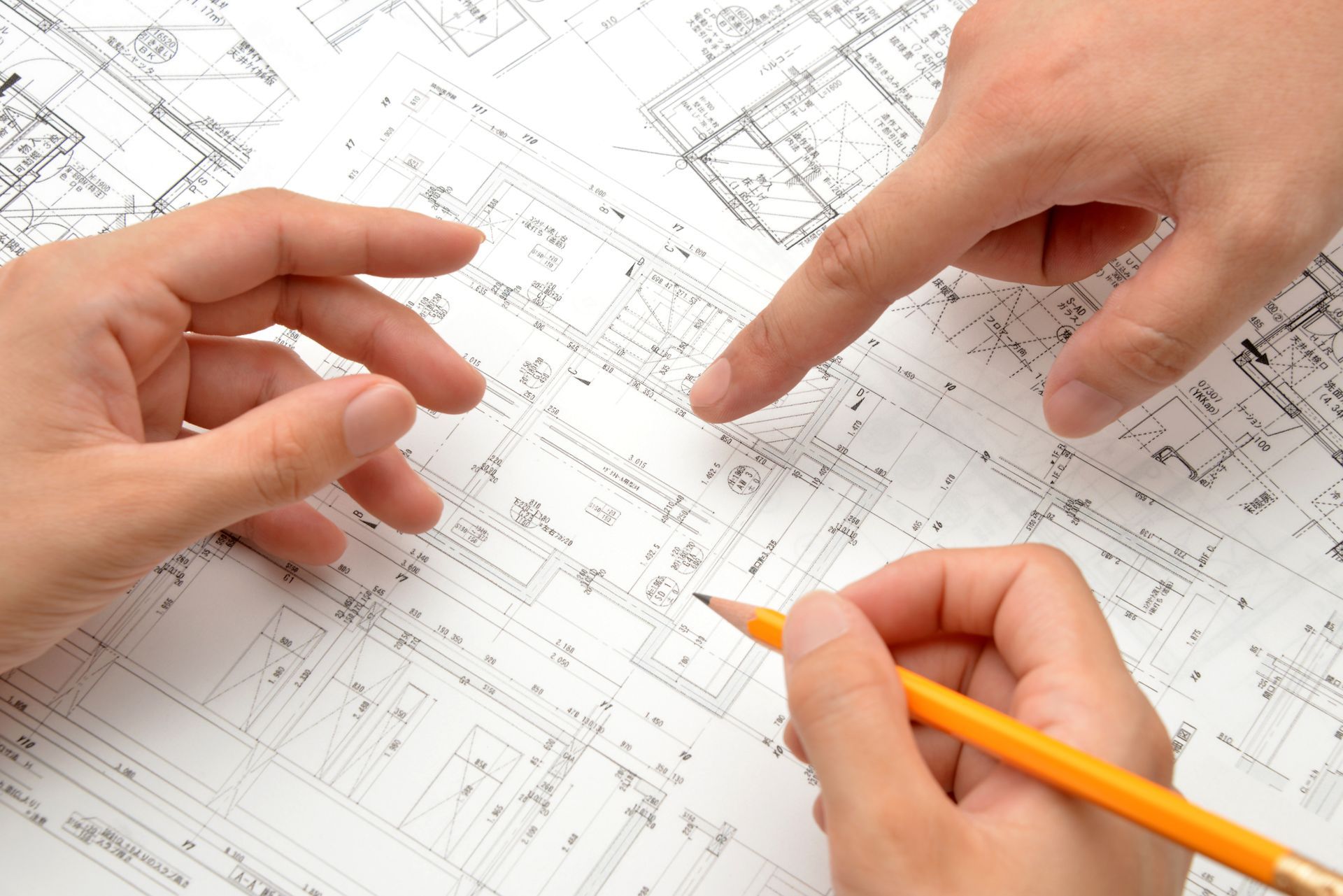Hands pointing at architectural plans during a quantity surveying discussion.