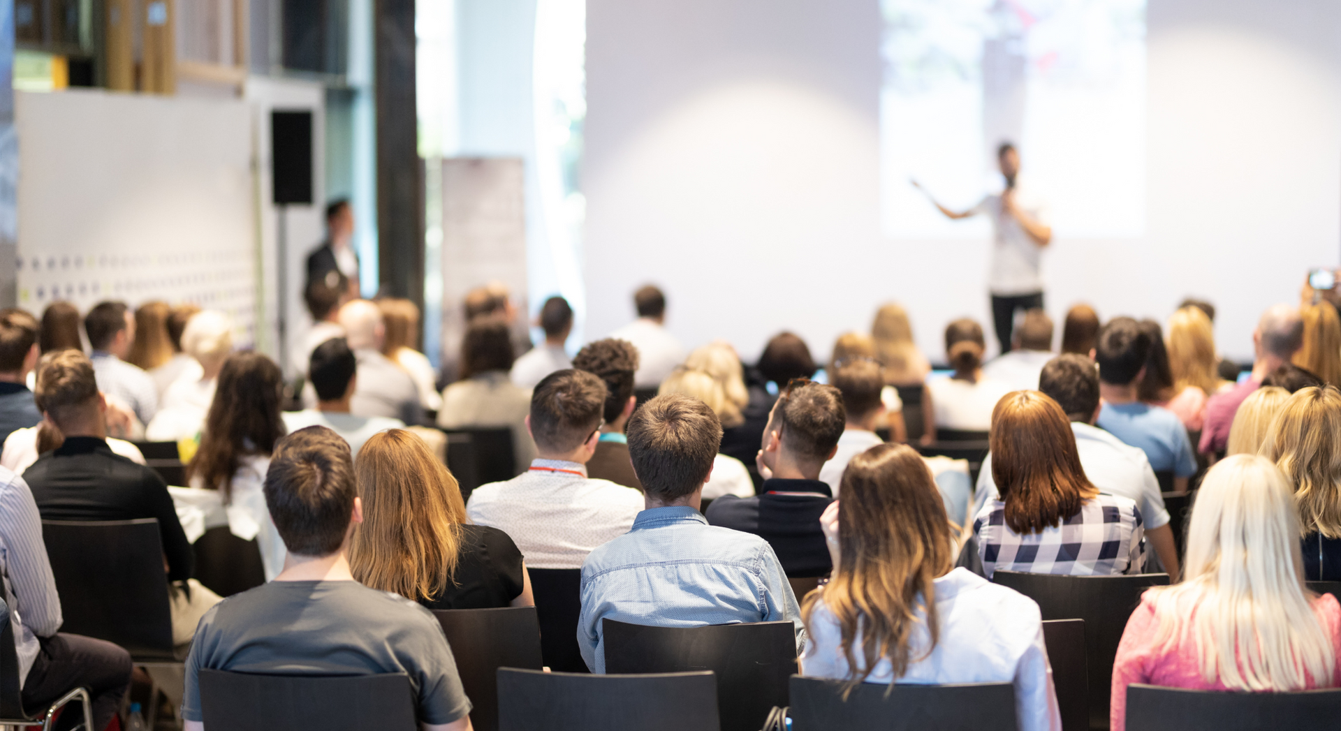 A large group of people are sitting in chairs in front of a man giving a presentation.
