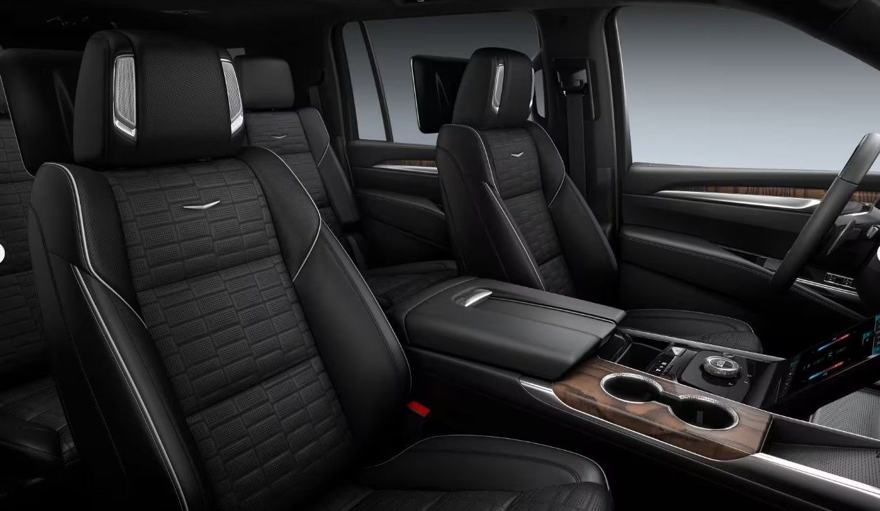 Interior of a luxury car featuring a large, curved display screen, white seats, and wood trim.