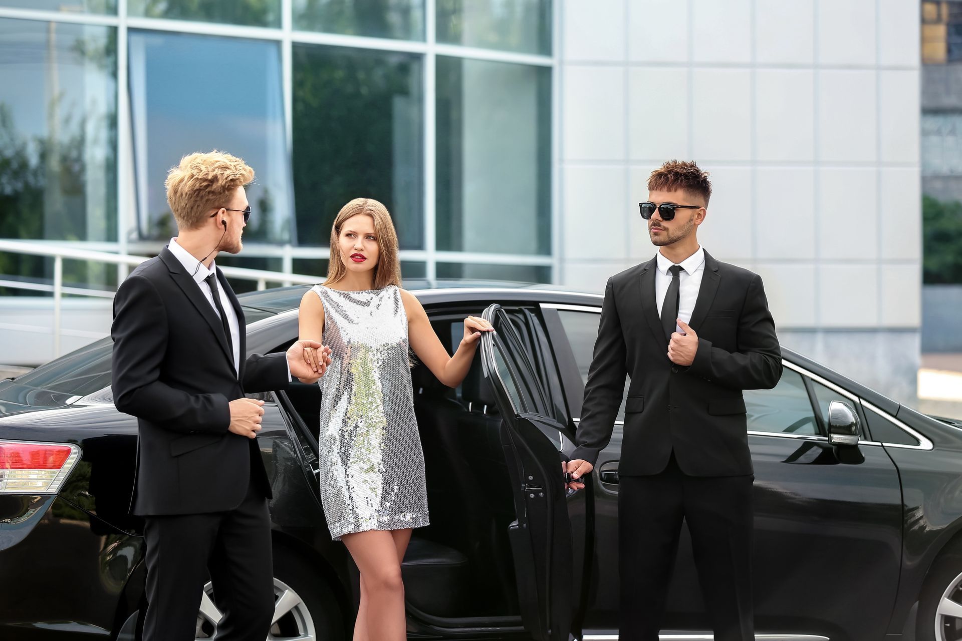 A woman is getting out of a limousine with two men standing next to her.