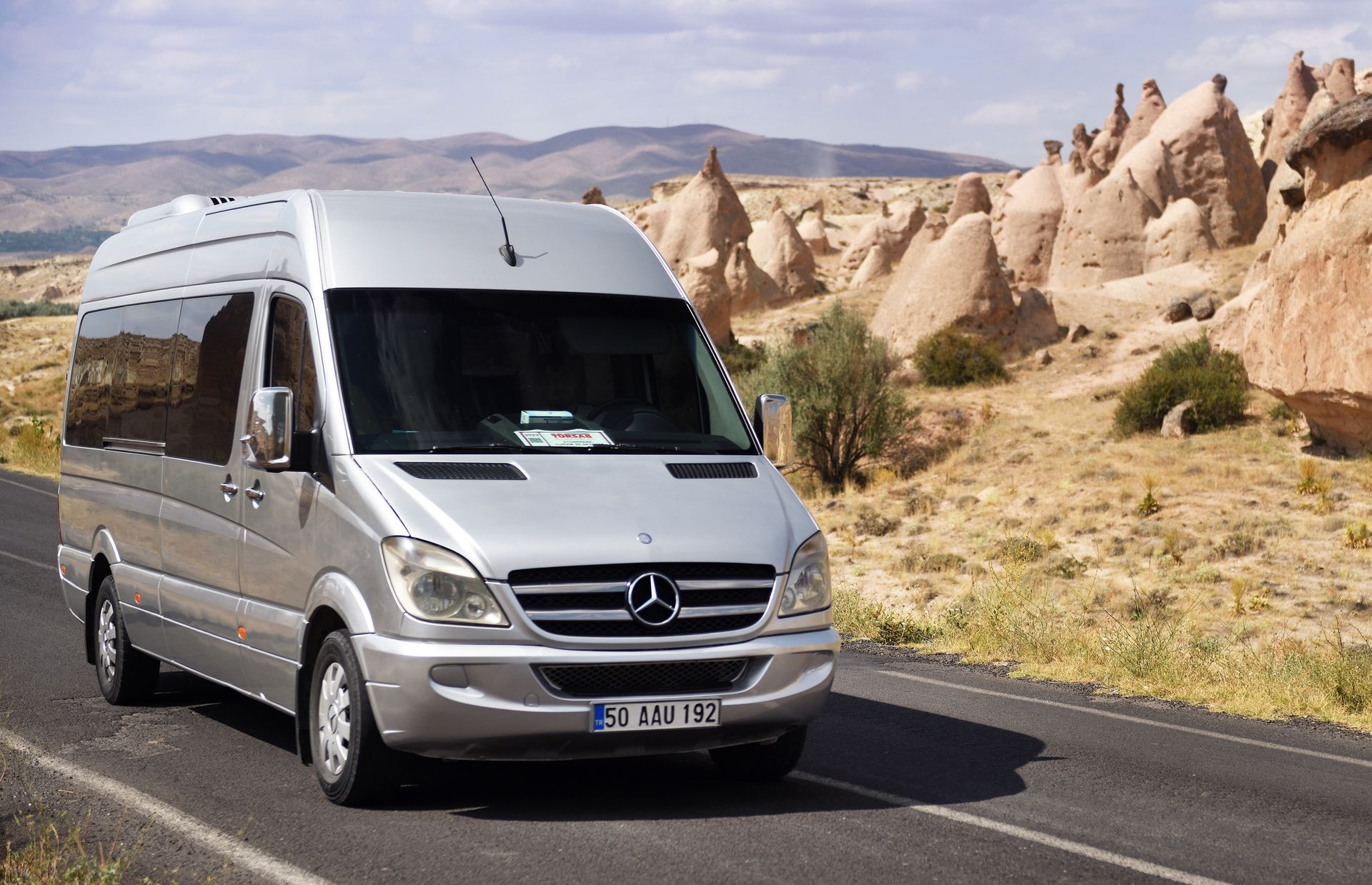 A silver mercedes van is driving down a desert road