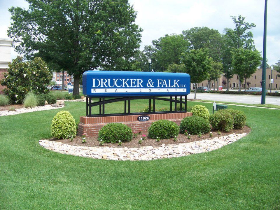 A sign for drucker & falk sits in the middle of a lush green field
