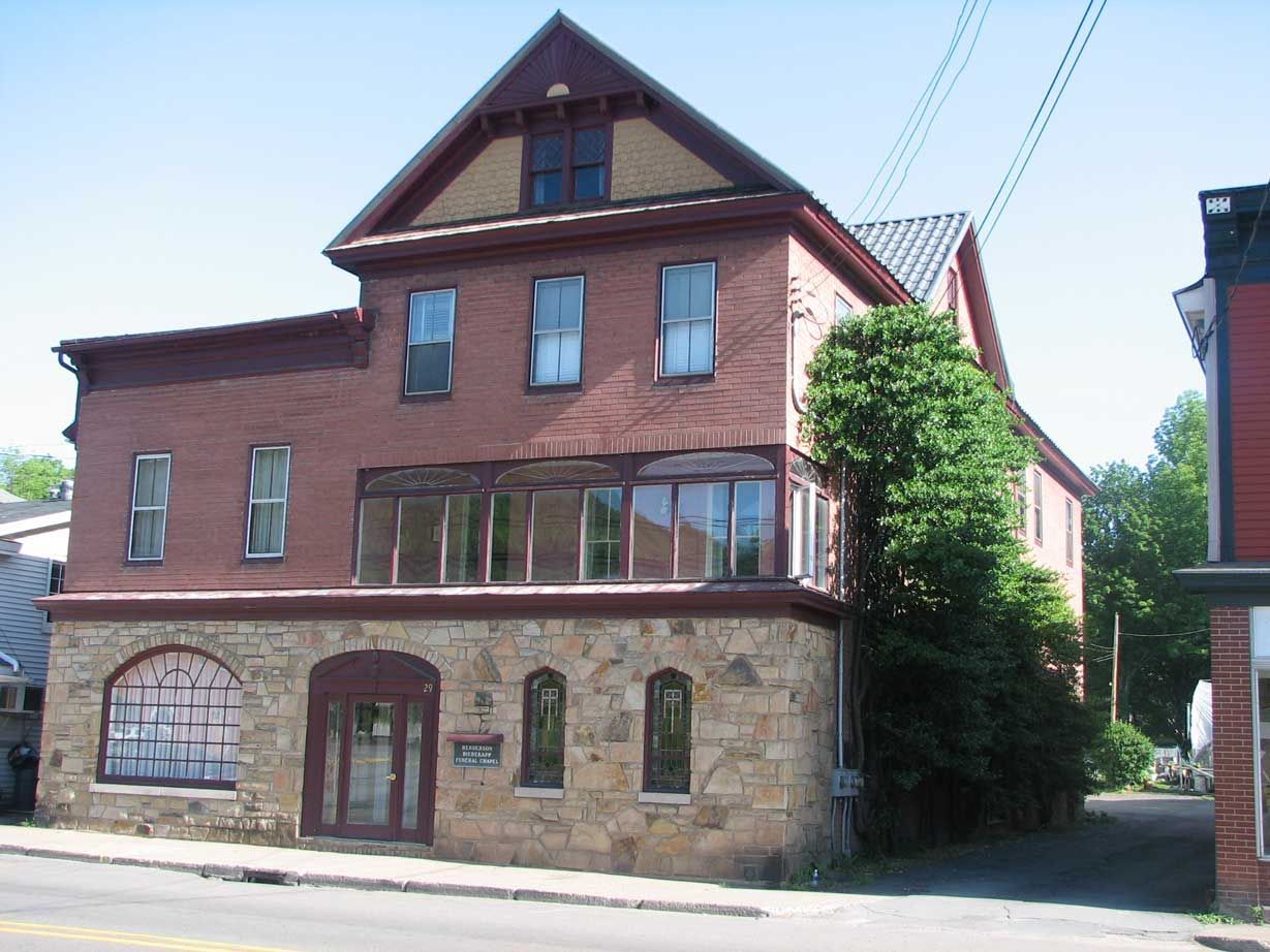 Three-story brick and stone building with a gabled roof and arched windows.