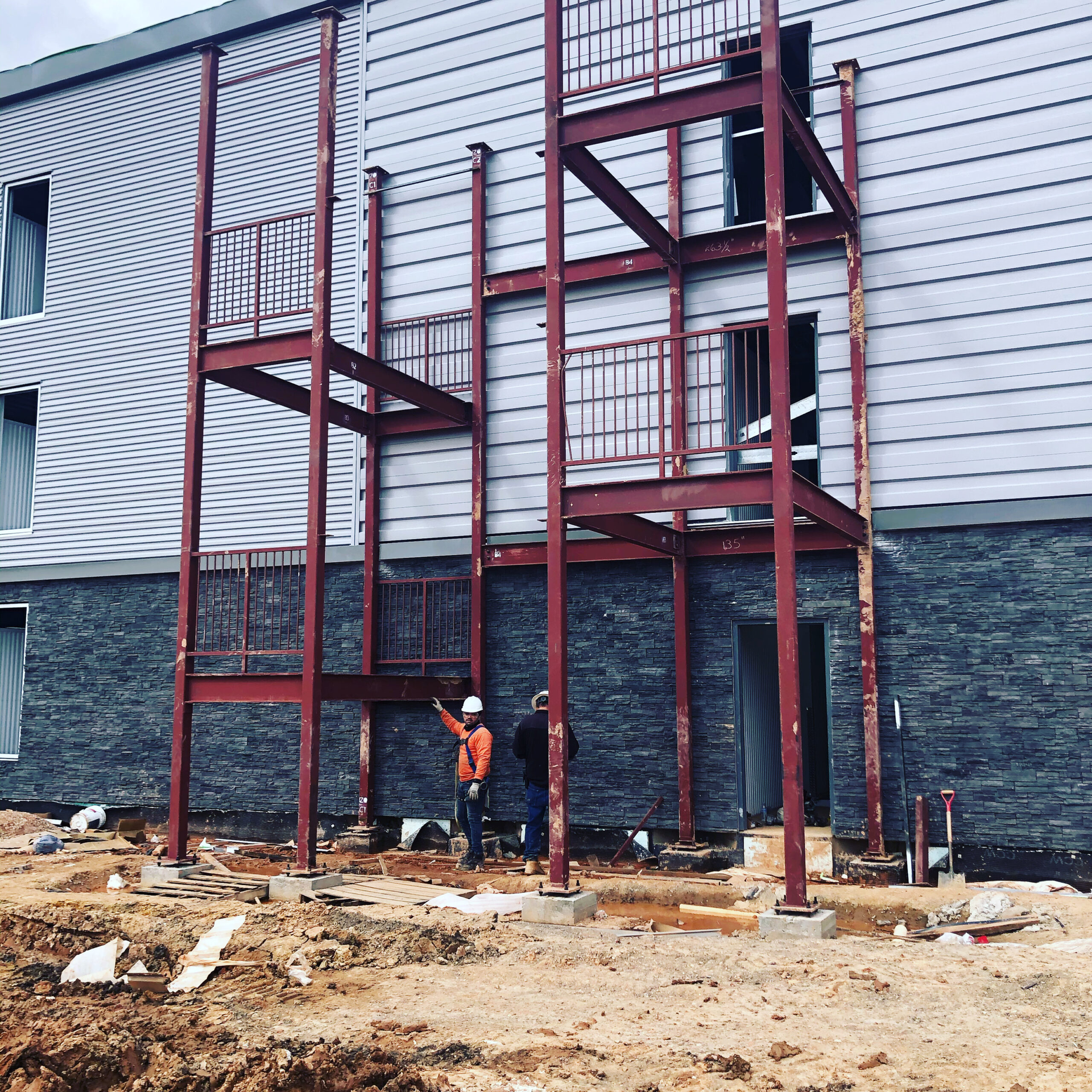 A man in a hard hat stands in front of a building under construction