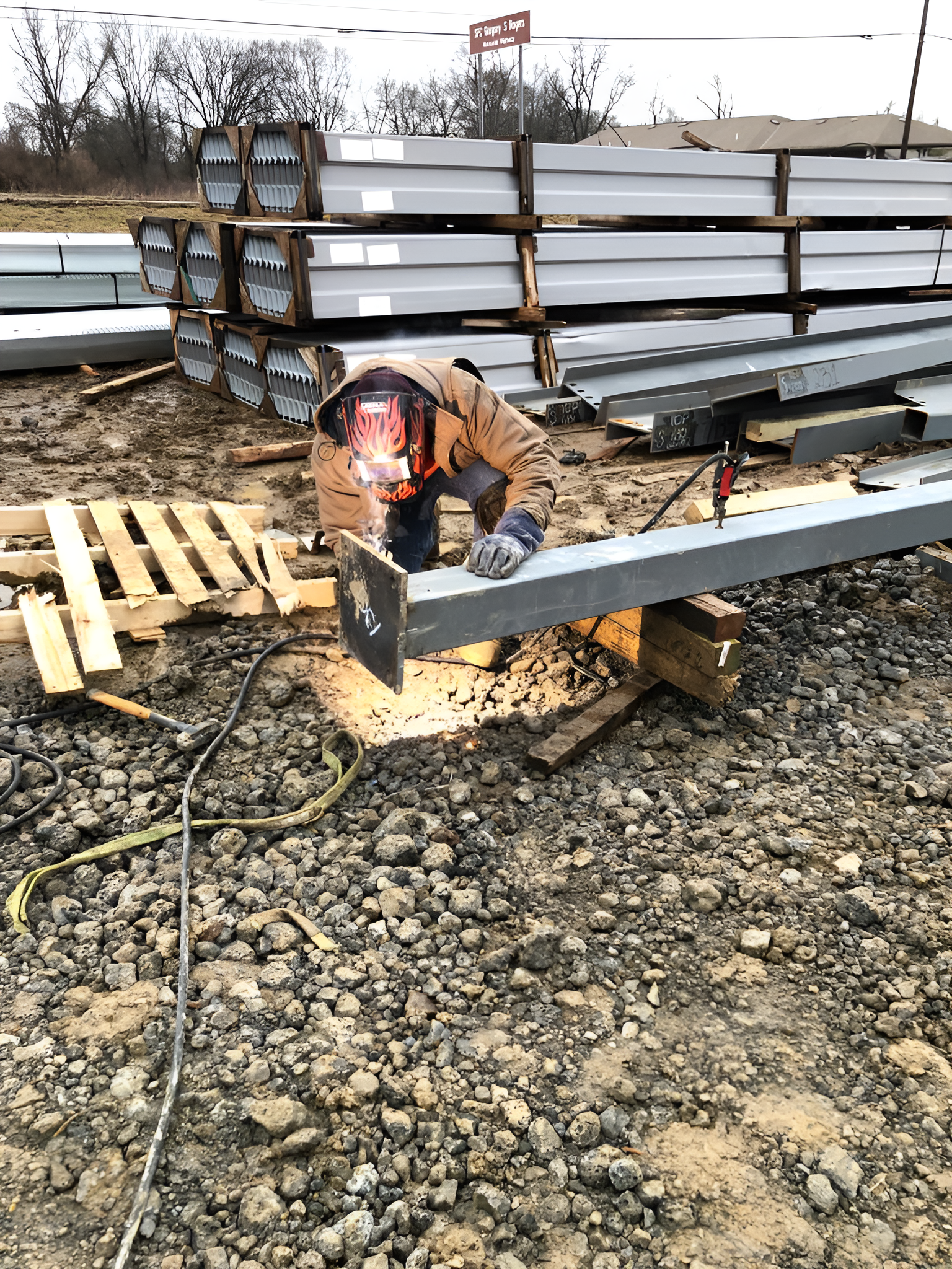 A man is welding a metal pole in a gravel area.