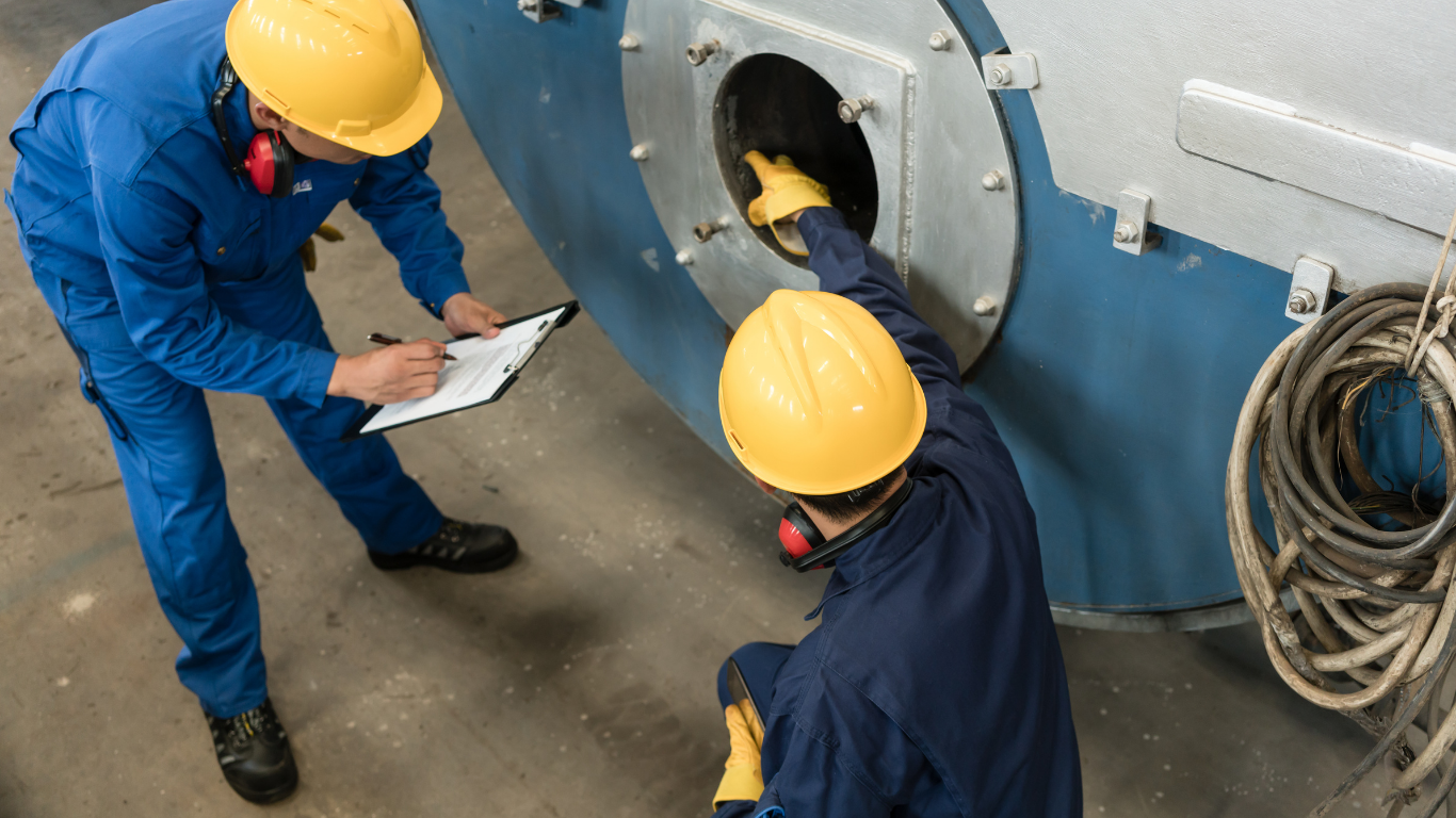 Two men in hard hats are working on a machine in a factory.