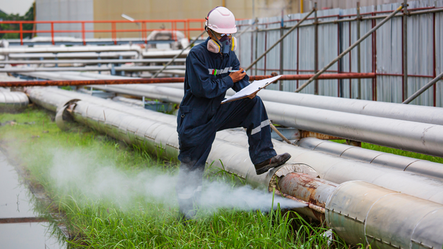 A man is kneeling on a pipe while looking at a clipboard.