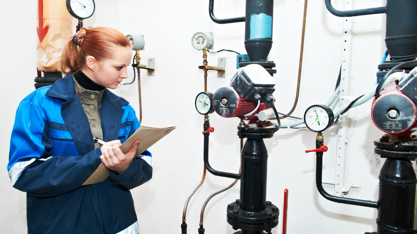 A woman is writing on a clipboard in a room with pipes.