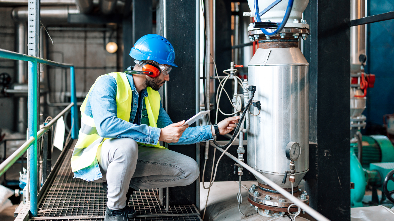 A man is kneeling down in a factory looking at a tablet.