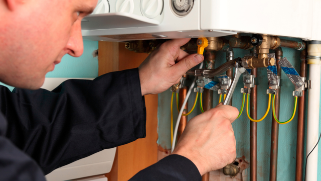 A man is fixing a boiler with a wrench.