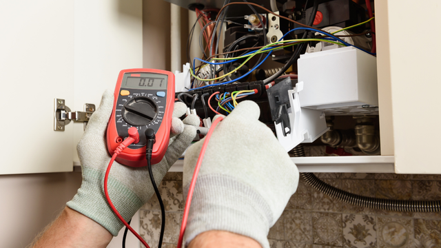 A person is using a multimeter to test an electrical box.