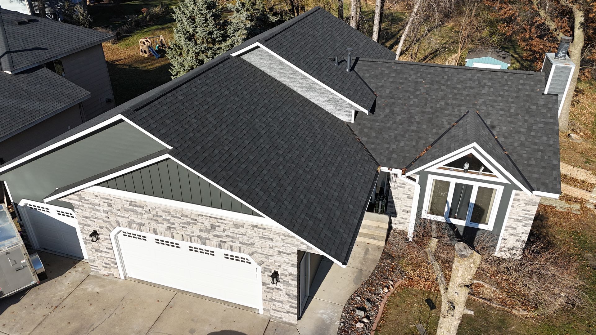 House with gray and black roof, stone facade, white garage door, and landscaping.
