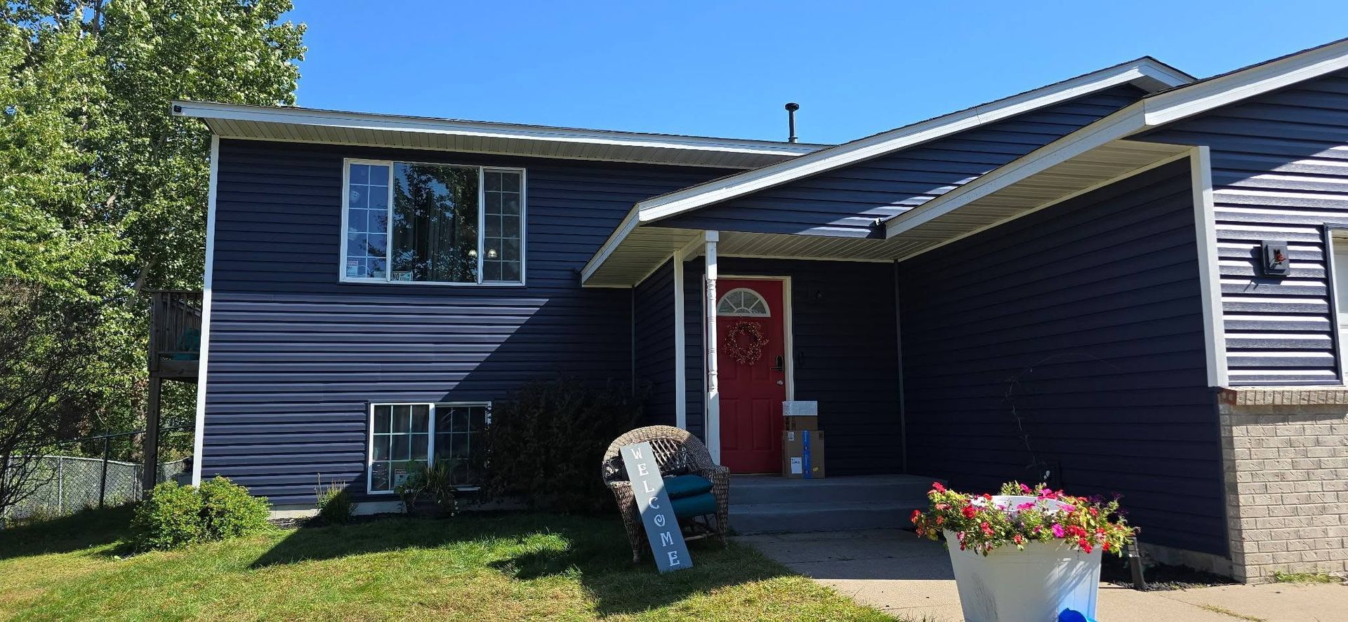 Dark blue house with a red door, white trim, and a flower pot on the porch.