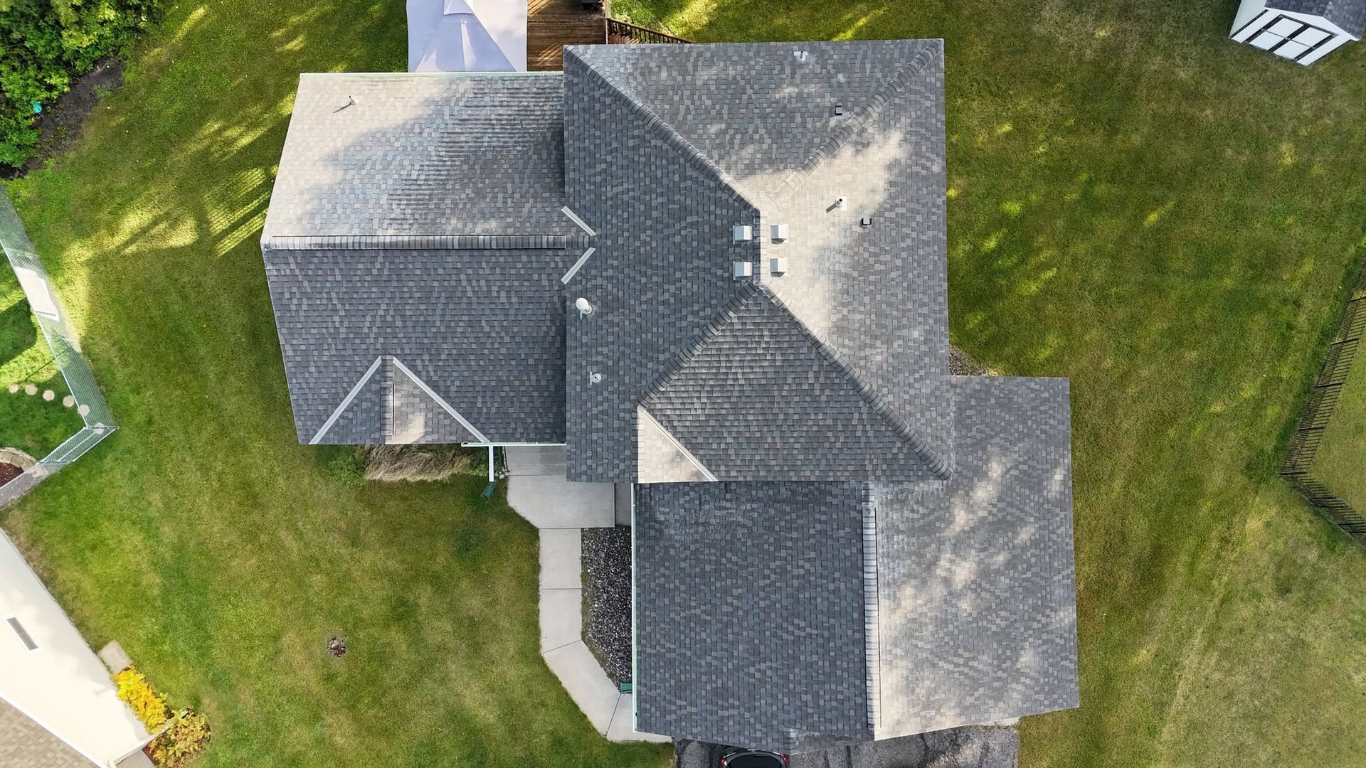 Overhead view of a house with a dark gray shingled roof surrounded by green grass.