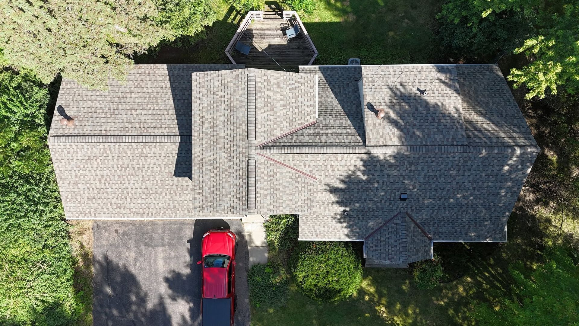 Overhead view of house with gray roof, red car in driveway, surrounded by green trees.