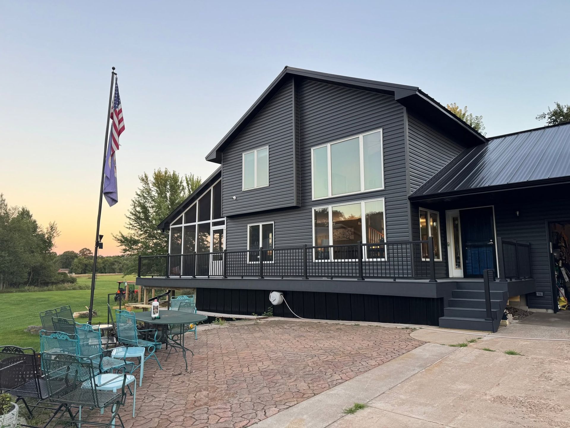 Two-story gray house with large windows, black trim, and a porch, with an American flag out front.