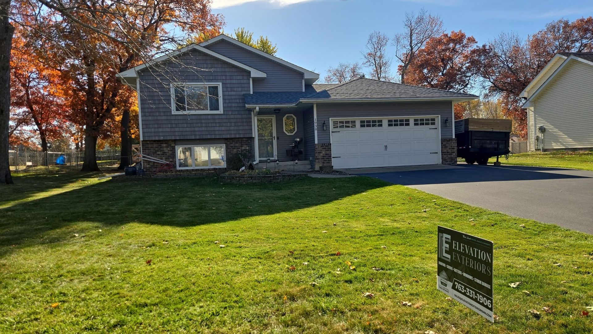 Gray house with a garage and a lawn. Sign in the yard.