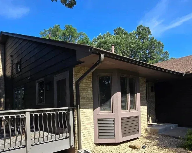 House exterior with brown siding, brick, and deck under a blue sky.