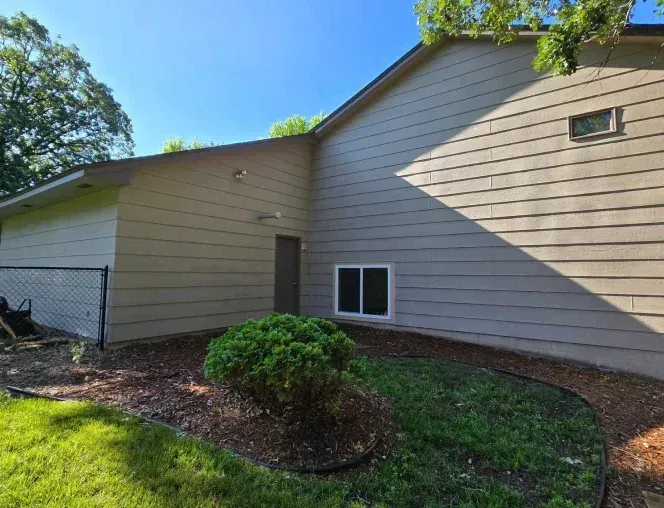 Beige house exterior with tan siding, a dark door, and a small, low hedge in a landscaped yard.