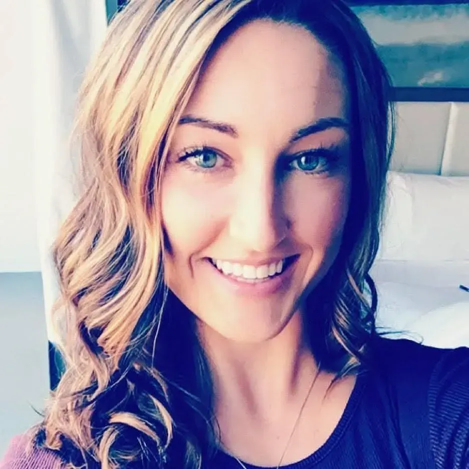 Woman with light brown hair smiles, blue eyes, wearing a dark purple shirt.