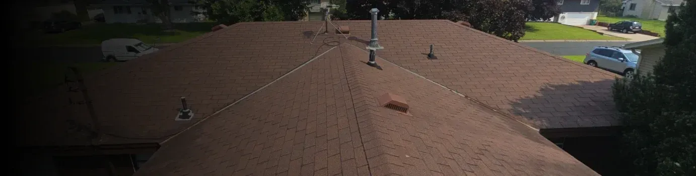 Brown shingle roof with chimneys, viewed from above, surrounded by trees and a neighborhood.