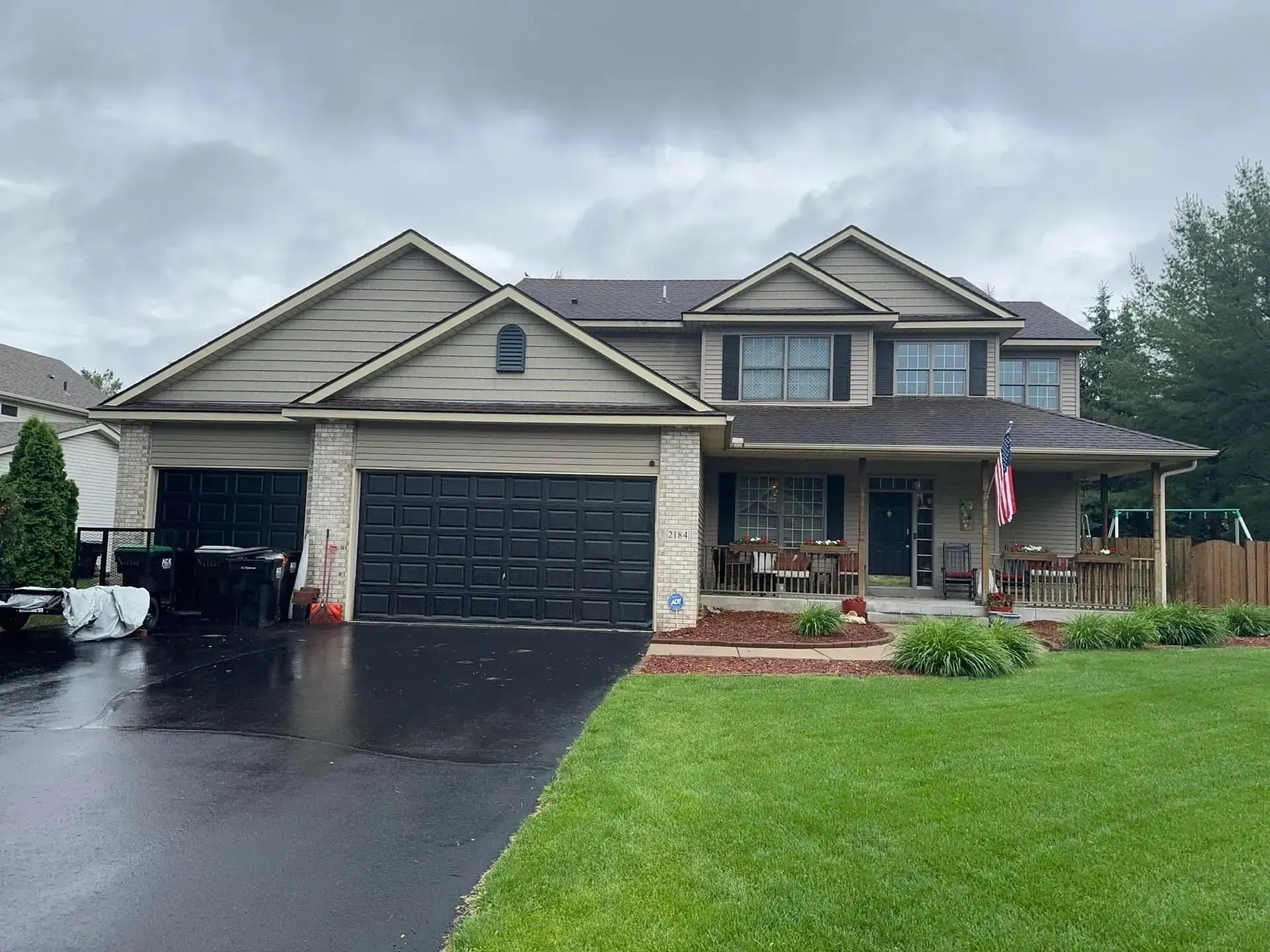 Two-story house with a black garage door and a covered porch; green lawn and cloudy sky.