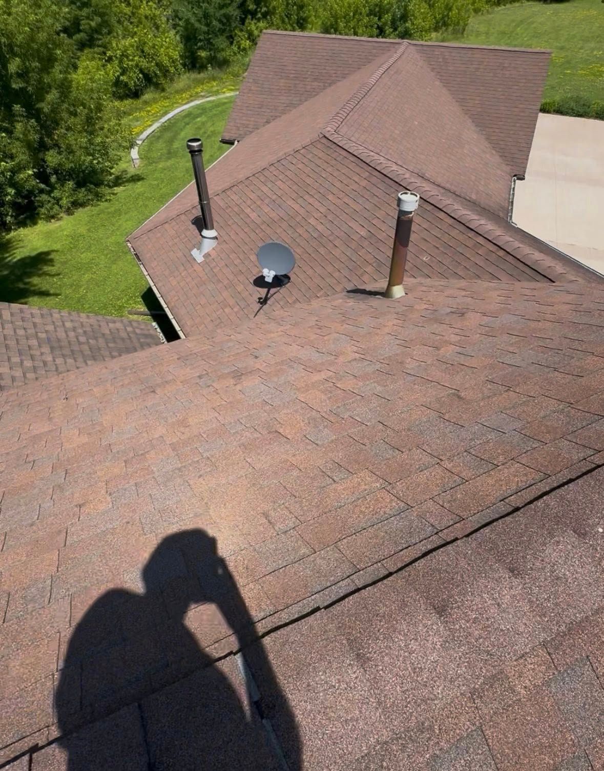 Brown shingled roof with chimneys and satellite dish, viewed from a high angle.