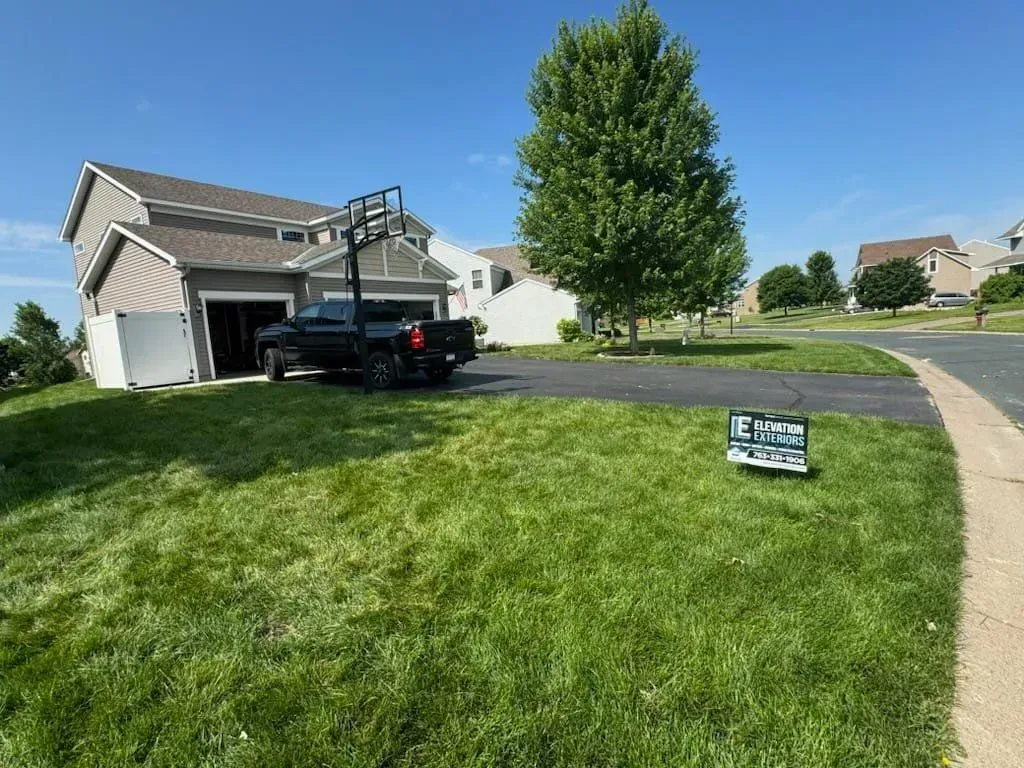 Black truck parked in front of a house with basketball hoop; sign on lawn; sunny day.