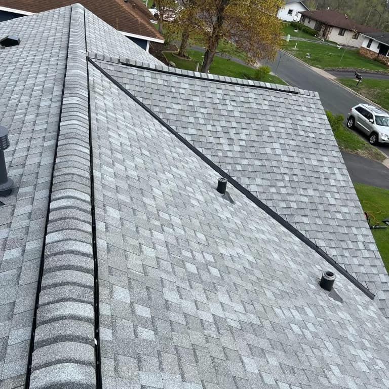 Overhead view of a gray shingle roof on a house, angled toward a street with a parked car and some green grass.