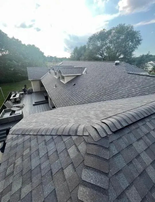 Gray shingle roof of a house with dormers, overlooking a wooden deck and trees.