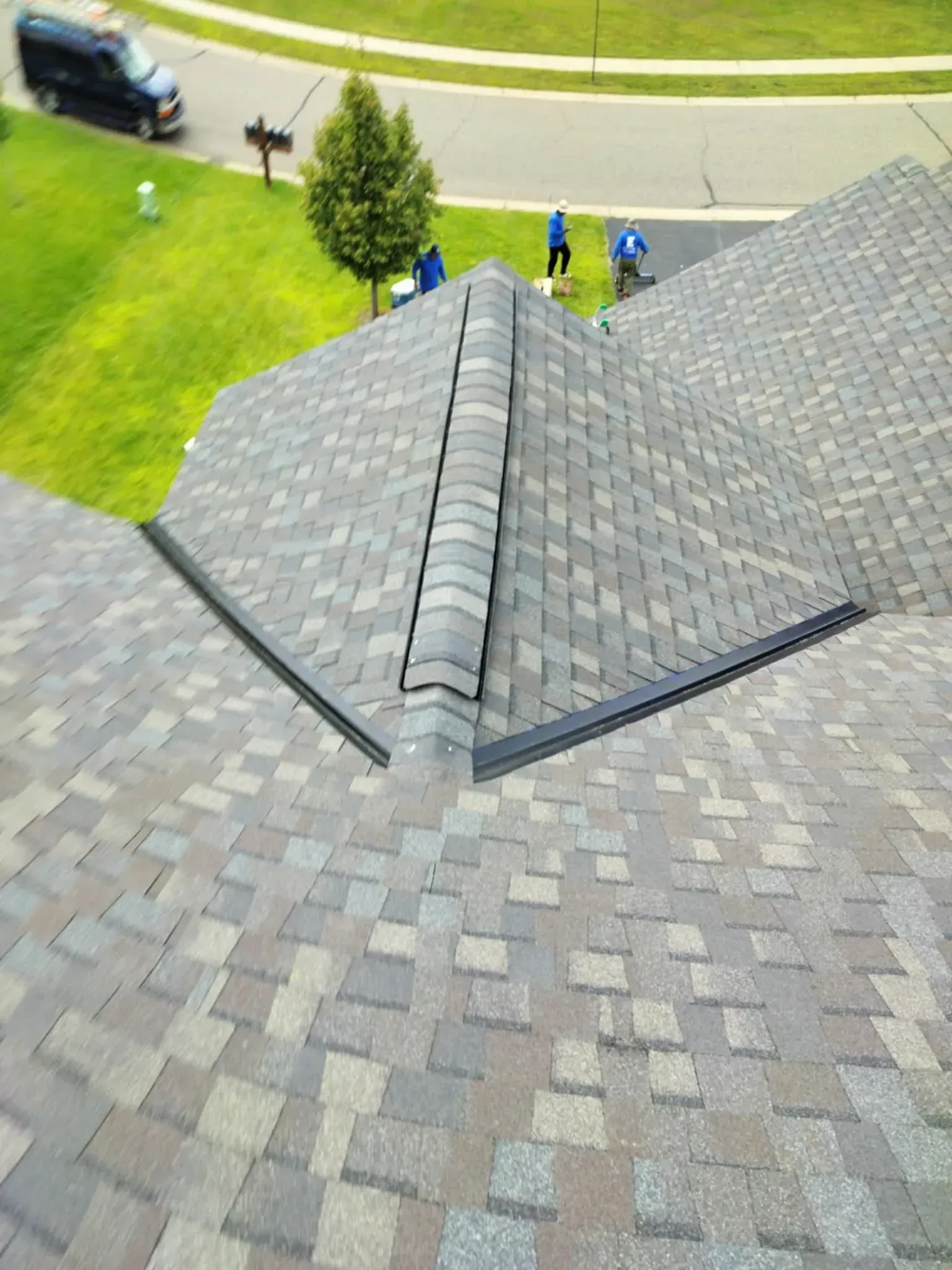 Roof with asphalt shingles and black metal flashing. Workers are visible on the roof.