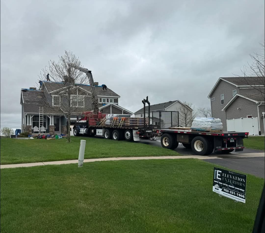 A flatbed truck delivering building materials to a house on a residential street. Overcast sky.
