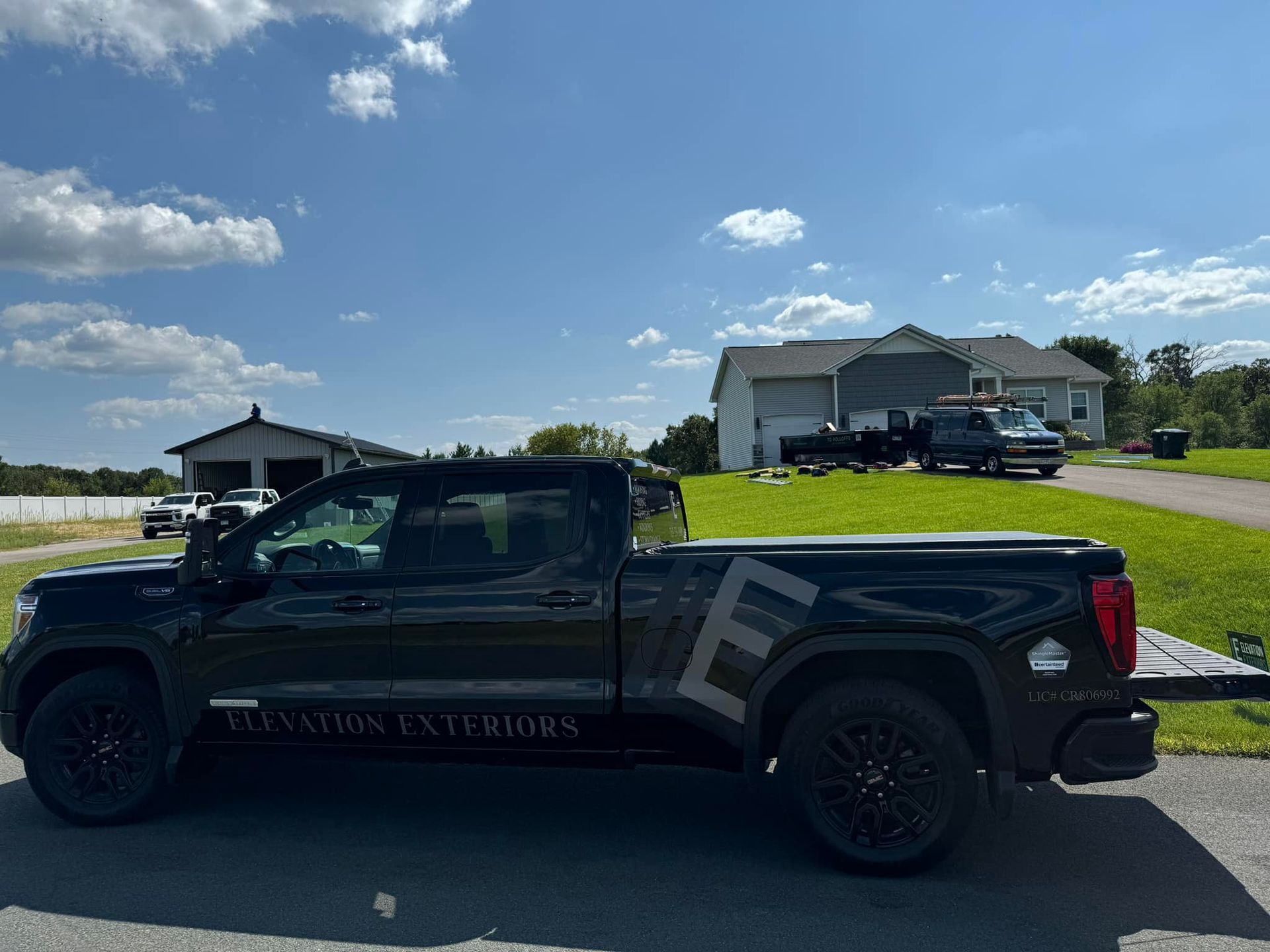 Black pickup truck with business logo parked on street, residential setting under blue sky.