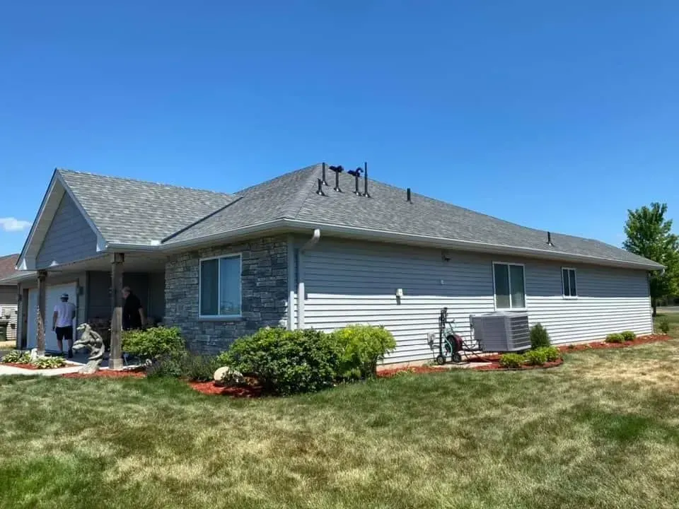 House with gray siding and roof, small bushes, blue sky, and green lawn.