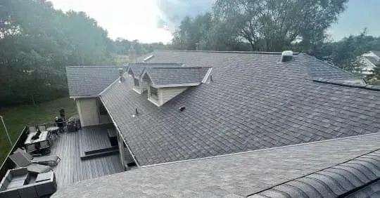 House roof with gray shingles, dormers, and deck, viewed from an elevated perspective.